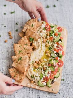 someone is placing tortilla chips on top of a wooden cutting board with vegetables and chickpeas