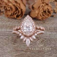 an engagement ring set with a pear shaped diamond surrounded by smaller round diamonds on a wooden surface