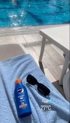 a bottle of sunscreen and sunglasses sitting on a towel next to a swimming pool