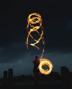 a person standing in front of a dark sky with fire spinning around their body and hands