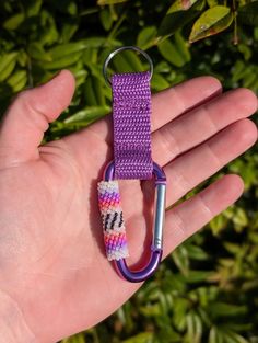 a hand holding a purple keychain with a metal hook