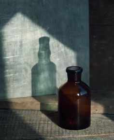 a brown glass bottle sitting on top of a wooden floor next to a shadow cast wall