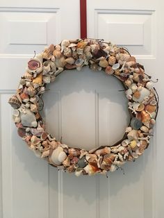 a wreath made out of seashells hangs on the front door with a red ribbon