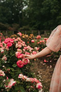 a woman in a pink dress is picking roses