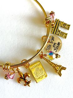 "Perfect souvenir of an enchanting trip to Paris, France. Adjustable gold plated bangle is highlighted with hand stamped quote \"La Vie en Rose\" and 5 detailed Parisian charms accented with rose colored Swarovski crystals AB.  Adjustable bangle is made of heavy gold plate over 1.8mm stainless steel. It is hypoallergenic and tarnish resistant. The diameter is 2 1/2\" to fit most.  Hand stamped 5/8\" 24 gauge shiny brass disc reads \"La Vie en Rose\". Two 6mm rose colored Swarovski crystals AB an Honeymoon Paris, Fun Halloween Earrings, Paris Charm Bracelet, Paris Souvenirs, Paris Bracelet, Bangle Bracelet Gold, Black Cat Earrings, Paris Trip, Pink Swarovski