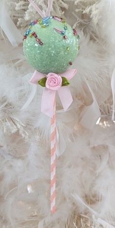 a green ornament hanging from a white christmas tree with pink and white ribbons