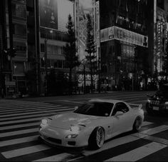 black and white photograph of two cars on the street in front of tall buildings at night