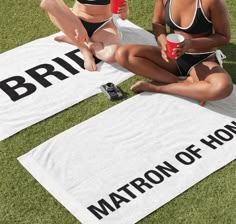 two women in bathing suits sitting on towels with drinks