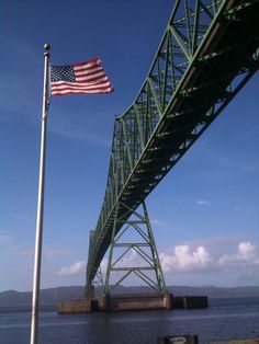 an american flag flying on the side of a green bridge over water with a blue sky in the background