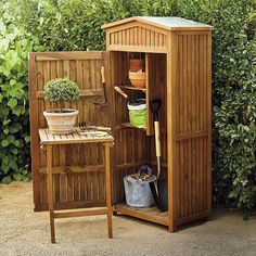 a wooden potting shed sitting in the middle of a garden with pots and gardening tools