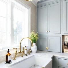 a white sink sitting under a window next to a counter top with gold faucets