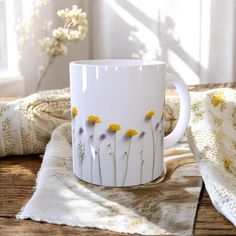 a white coffee mug with yellow and purple flowers painted on the side sitting on a table