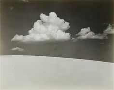 an old black and white photo of clouds in the sky over a snow covered field