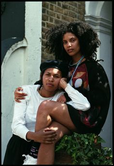 two women sitting on top of each other in front of a building