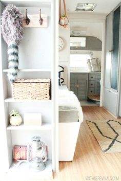 a white book shelf filled with lots of items next to a bed and kitchen area