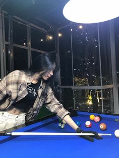 a woman leaning over a pool table in front of a window with balls on it