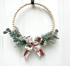 a wooden beaded wreath hanging on a white door with greenery and bells attached to it