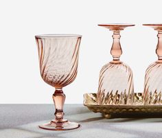 three pink glass goblets sitting on a tray