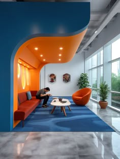 a man sitting on a couch in a room with blue carpet and orange walls, looking at his laptop