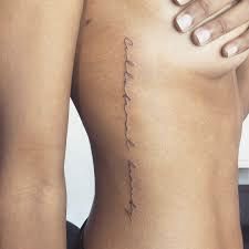 the back of a woman's body with her hand on her shoulder and writing on it