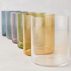 four different colored glass vases lined up on a white surface, one is empty