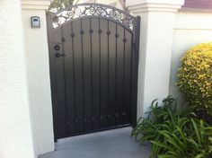 an iron gate is open on the side of a white house with yellow flowers in front