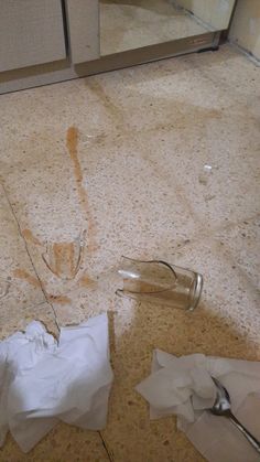 the floor is littered with toilet paper and broken glass bottles on it, including one that has been left open