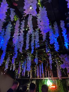 purple and blue flowers hanging from the ceiling in a restaurant or bar with people sitting at tables