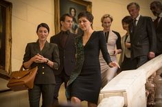 two women walking down the stairs with other people in suits and ties behind them, one woman is carrying a brown purse