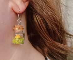 there is a small glass jar with moss in it hanging from the back of a woman's ear