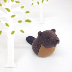 a stuffed animal beaver sitting next to a tree with leaves on it's branches