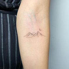 a woman's arm with a small mountain tattoo on the back of her left arm