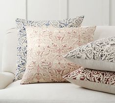 three pillows on a couch with white walls in the background and blue, red, and beige colors