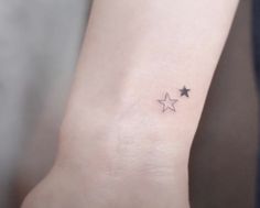 a small star tattoo on the wrist is shown in black and grey ink, with three smaller stars above it