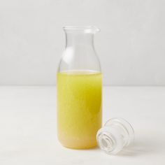 a glass bottle filled with yellow liquid next to an empty container on a white surface