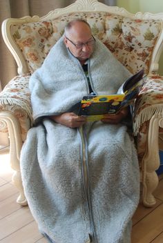 a man sitting in a chair with a blanket on top of his lap reading a book