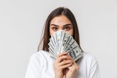 a woman covering her face with one hundred dollar bills