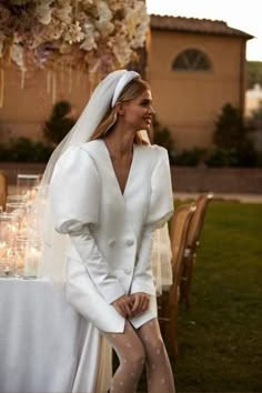 a woman wearing a white dress and veil standing in front of a table with candles