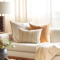 a living room with a white couch and some pillows on top of the couch next to a window