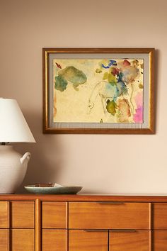 a painting hanging on the wall above a dresser with a vase and lamp next to it