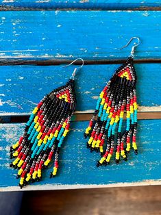 two pairs of colorful beaded earrings sitting on top of a blue wooden bench next to each other