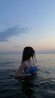 a woman is sitting in the water looking out at the ocean while wearing a blue bathing suit