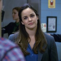 a woman in a blue shirt and blazer looking at another person with one hand on her hip