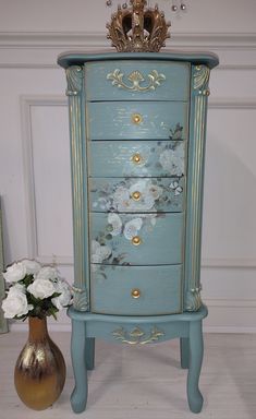 a blue dresser with flowers on it next to a vase