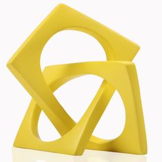 a yellow sculpture sitting on top of a white table next to a black object in the shape of a triangle