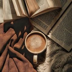 a cup of coffee sitting on top of a blanket next to two open book's