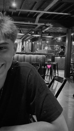 a young man sitting at a table in a restaurant smiling for the camera with his hand on his chin