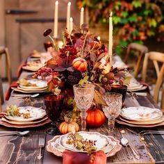 the table is set with candles, plates and pumpkins for thanksgiving dinner guests to enjoy