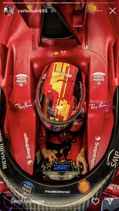 a man in a red race car with his hands on the steering wheel and looking down