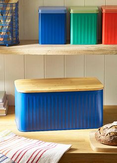 three different colored containers sitting on top of a wooden table next to a loaf of bread